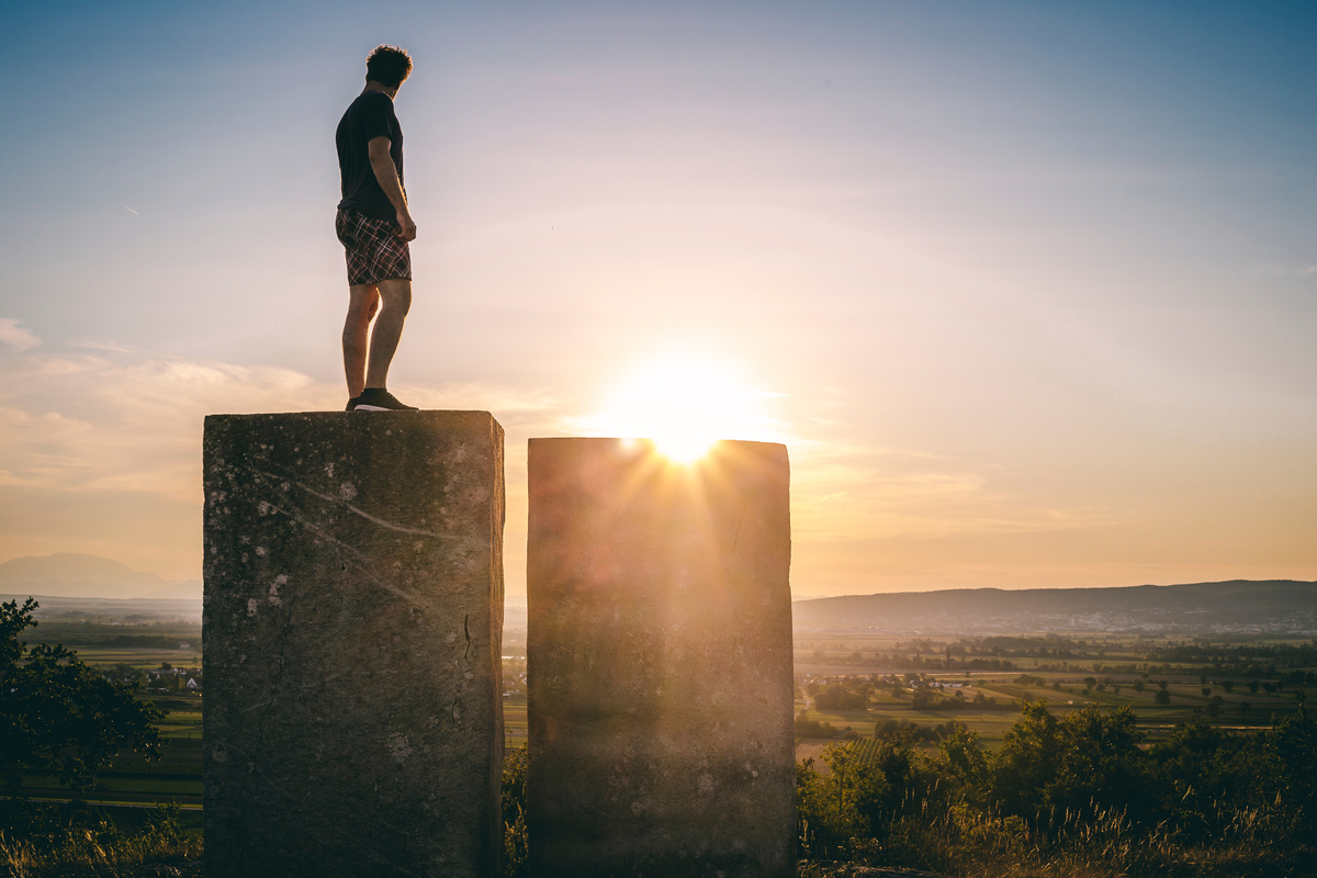 Man in Black Shirt Standing on Rock during Sunset